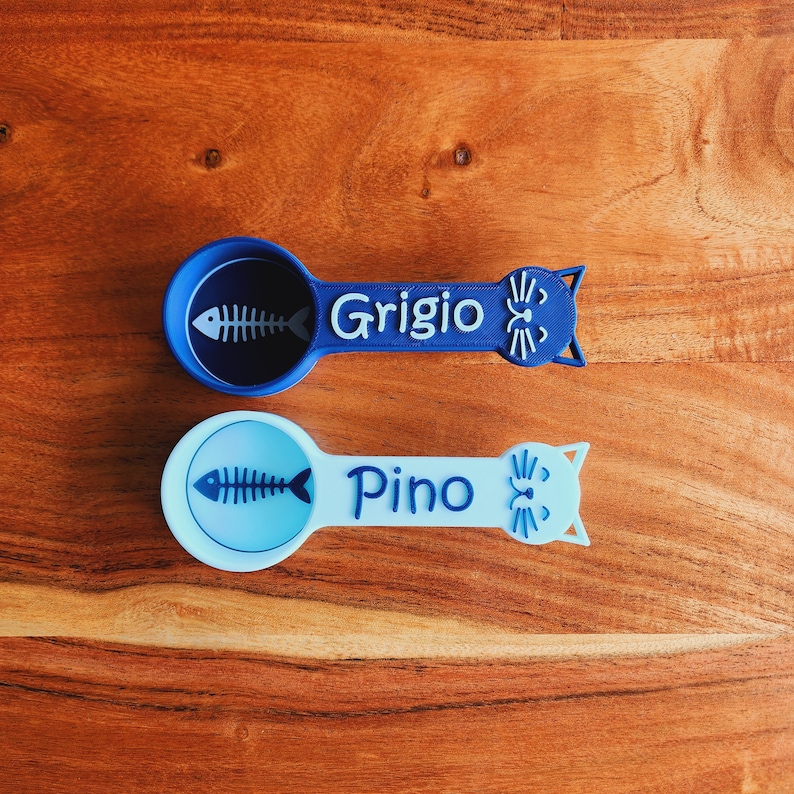 May include: Two blue and light blue cat-shaped spoons with fishbone designs. The blue spoon says "Grigio" and the light blue spoon says "Pino".