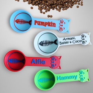 May include: Four colorful cat-shaped measuring spoons with fishbone designs. The spoons are labeled "Pumpkin", "Alfie", "Hammy", and "Armani, Bailey & Coco".