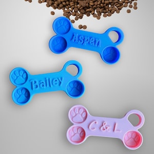 May include: Three personalised dog bone shaped treat dispensers. One is blue with the name Bailey, one is blue with the name Aspen, and one is pink with the name C&L.