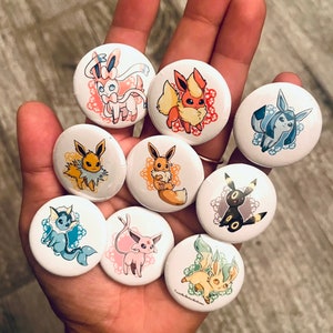 May include: Nine round buttons featuring different Pokemon characters. The buttons are white with a colorful design of each Pokemon character. The characters include Eevee, Flareon, Vaporeon, Jolteon, Espeon, Umbreon, Glaceon, Leafeon, and Sylveon.