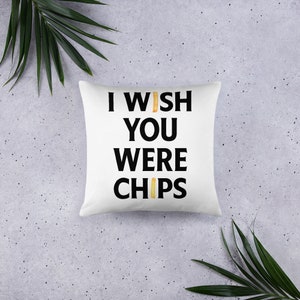 Könnte beinhalten: Ein weißes Kissen mit schwarzem Text, der "I wish you were chips" lautet, wobei zwei gelbe Pommes Frites die "I" und "S" im Text ersetzen.