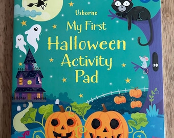 May include: A colorful Halloween-themed activity pad with the title "My First Halloween Activity Pad" by Usborne. The cover features a witch, ghosts, a black cat, jack-o'-lanterns, and a haunted house. The background is a dark blue with stars.