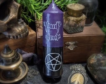 May include: Purple and black candle with a pentagram and fangs design. The candle is surrounded by various occult objects, including a skull, a censer, and a necklace.