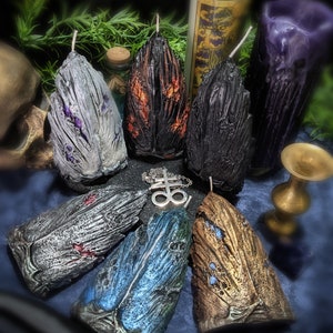 Puede incluir: Un conjunto de siete velas con forma de alas, cada una con un color y una textura diferentes. Las velas están dispuestas en círculo sobre una superficie azul. Las velas están hechas de cera y tienen un aspecto natural y rústico.