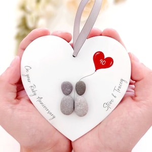 May include: White heart-shaped wooden plaque with a red heart balloon with the number 40 on it. Two grey painted pebbles are holding hands. The text "On your Ruby Anniversary" and "Steve & Tracey" are written on the plaque.