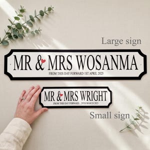 May include: Two personalized wedding signs, one large and one small, with black borders and white backgrounds. The signs read "MR & MRS WOSANMA" and "MR & MRS WRIGHT" with dates. A red heart is between the "MR" and "MRS".