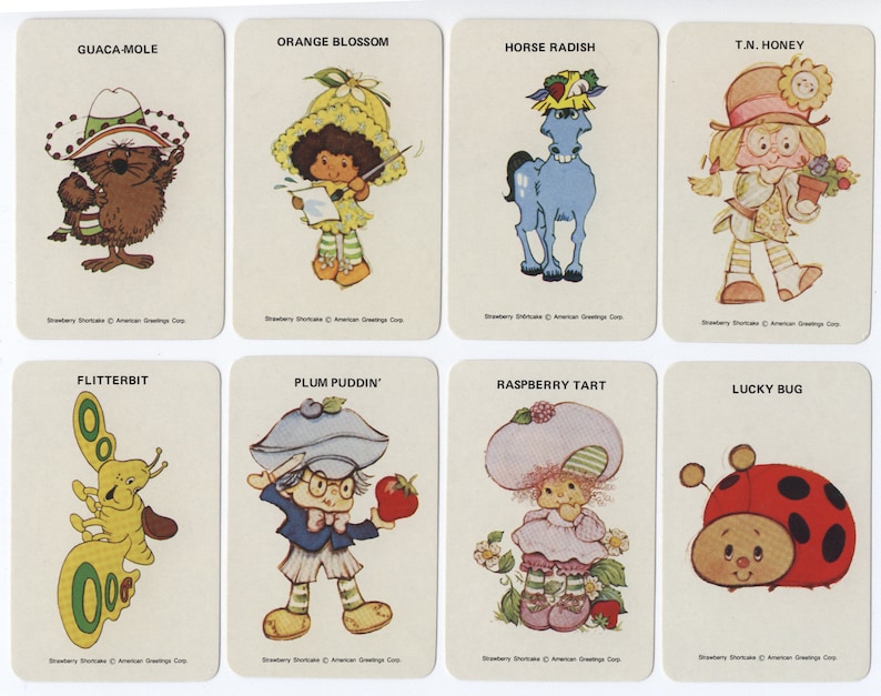Op de afbeelding: Een set van acht Strawberry Shortcake-personagekaarten. Elke kaart heeft een ander personage met een unieke naam en een kleurrijke illustratie. De personages zijn Guaca-Mole, Orange Blossom, Horse Radish, T.N. Honey, Flitterbit, Plum Puddin', Raspberry Tart en Lucky Bug.