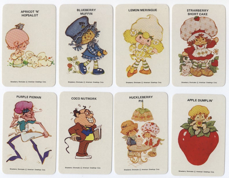 Op de afbeelding: Een set van acht Strawberry Shortcake-personagekaarten. Elke kaart toont een ander personage met zijn naam en een korte beschrijving. De personages zijn: Apricot 'n' Hopsalot, Blueberry Muffin, Lemon Meringue, Strawberry Shortcake, Purple Pieman, Coco Nutwork, Huckleberry Pie en Apple Dumplin'.