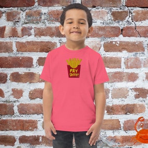 May include: A pink t-shirt featuring a graphic of a red and yellow french fry container with the text "Fry Day!" printed on it.