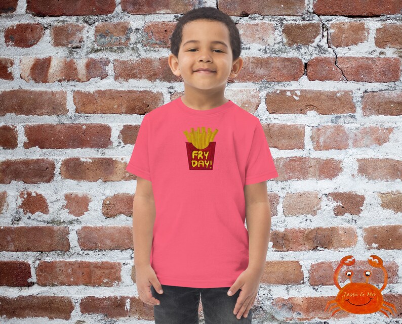 May include: A pink t-shirt featuring a graphic of a red and yellow french fry container with the text "Fry Day!" printed on it.