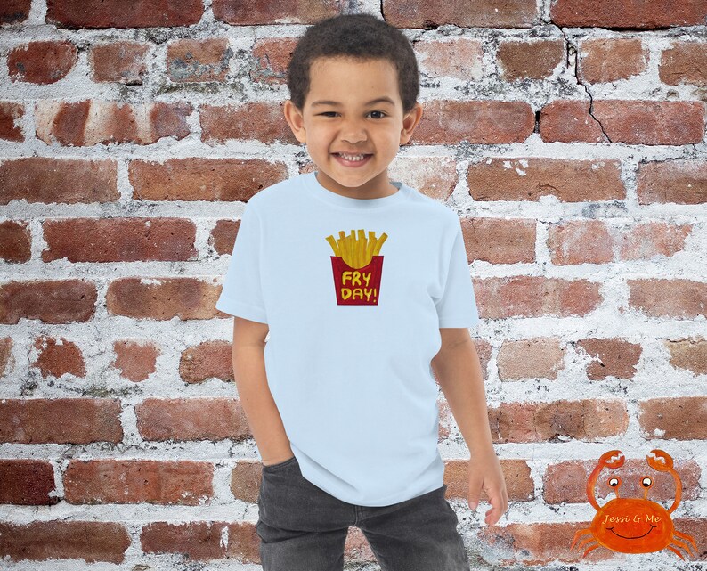 May include: A light blue t-shirt with a red and yellow graphic of french fries in a red container with the text "Fry Day!" printed on it.