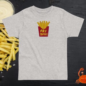 May include: Grey t-shirt with a red box and the text "Fry Day!" inside. The box contains a cartoon image of chips.