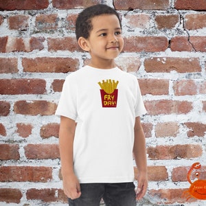 May include: White t-shirt with a red and yellow graphic of french fries in a red container with the text "Fry Day!" printed on the front.
