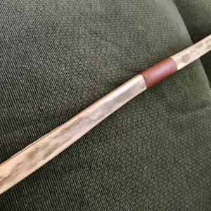 May include: A wooden bow with a brown leather grip. The bow is made of natural wood with a light brown color and a smooth finish.