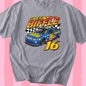 May include: A grey t-shirt with a graphic of a blue race car, number 16, and the name "Greg Biffle." The car has stars and the words "National Guard." The design includes flames and a chequered flag.