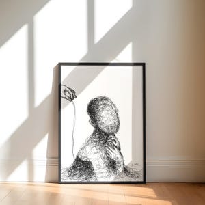 May include: Black and white framed art print featuring a line drawing of a person with a scribbled face and body. A hand holding a string is above the person's head. The artwork is displayed on a white wall with a shadow.
