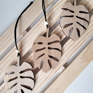 May include: Three wooden monstera leaf ornaments with black cords and white beads hanging on a wooden slat wall.