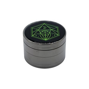 Op de afbeelding: Een metallic grijze kruidenmolen met een zwarte bovenkant met een neon groen geometrisch ontwerp. De molen heeft een driedelige constructie en een geribbelde buitenkant voor grip. Het ontwerp omvat een oog, maan en sterren.