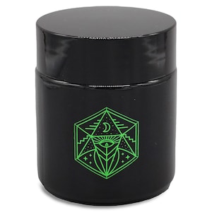 May include: Black glass jar with a green geometric design featuring a crescent moon, eye, and stars. The design is reminiscent of a mystical or spiritual symbol.