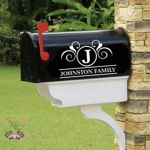 May include: Black mailbox with a white and black decal. The decal features the letter "J" inside a circle, with the words "JOHNSTON FAMILY" below. The mailbox has a red flag and a white base.