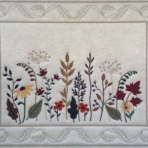 Può includere: Arte da parete ricamata con un motivo floreale in varie tonalità di rosso, giallo, marrone e verde. I fiori sono circondati da un bordo decorativo.