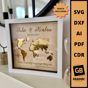 May include: A framed wooden world map with gold foil continents. The white frame surrounds a beige background with the names "Julie & Kealan" and the date "04.06.2025". The text "Your journey together begins" is also included.