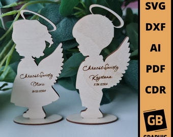 May include: Two wooden angel figurines with halo and wings. The figurines are personalized with the text "Chrzest Swięty" followed by a name and date. The text is engraved in brown on the light brown wood.