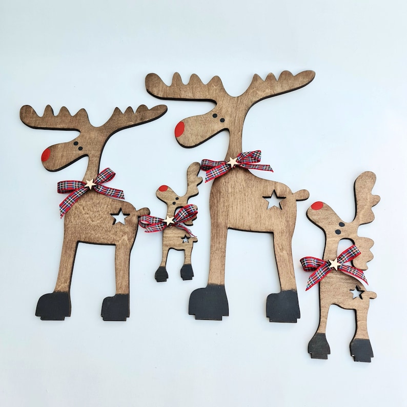 Set of four stained wooden reindeer figures of different sizes arranged on a white surface with star cutouts, red noses, and tartan ribbon bows, displayed next to vector format tags.