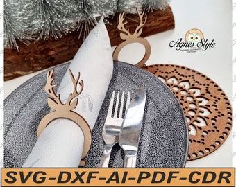 May include: Wooden reindeer napkin rings with a brown finish. The rings are placed on a white napkin and a black plate. A wooden coaster with a decorative design is in the background.