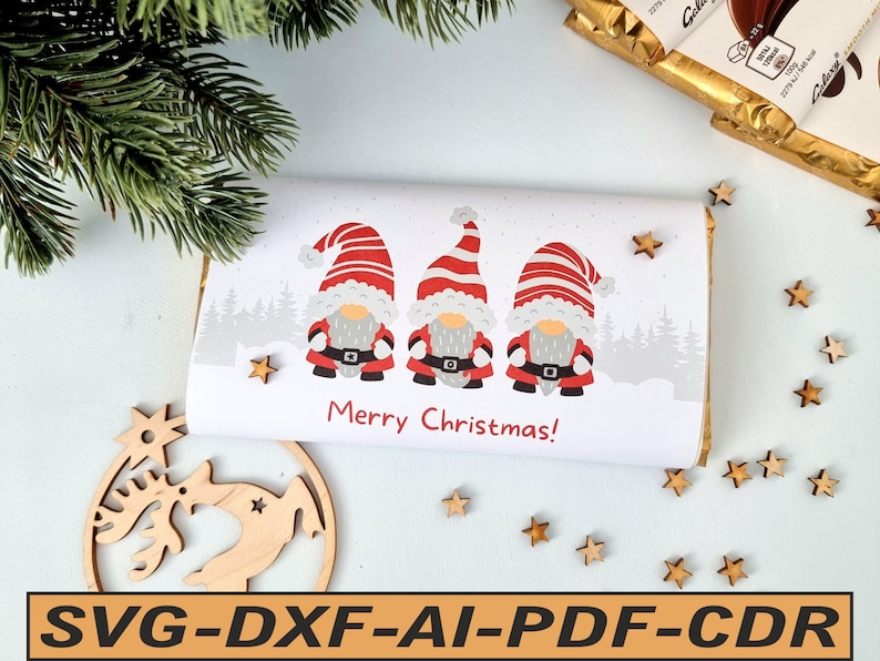 Printed Christmas chocolate bar wrapper featuring three red-hatted gnomes wrapped around a Galaxy 110g chocolate bar on a white surface with pine branches and wooden stars, shown with file format tags.