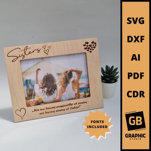 May include: A wooden photo frame with a heart design and the text "Sisters" and a quote in Polish. The frame is light brown and has a cutout for a photo. The quote reads "Nie ma lepszej przyjaciółki od siostry ani lepszej siostry od Ciebie!"