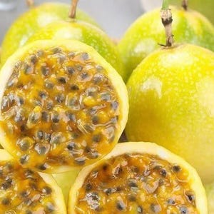 May include: Close-up of several passion fruits, some whole and others sliced open. The fruits are a vibrant yellow-green color with a textured skin. The inside of the sliced fruits reveals a juicy, yellow pulp filled with numerous dark seeds. The image highlights the tropical fruit's unique appearance.