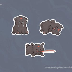 May include: Set of three vinyl holo stickers featuring a cartoon dog in various poses. The dog is dark gray with a red heart on its forehead. One sticker shows the dog crying, another lying down, and the last with a red sword. The text "2 inch vinyl holo stickers" is at the bottom.