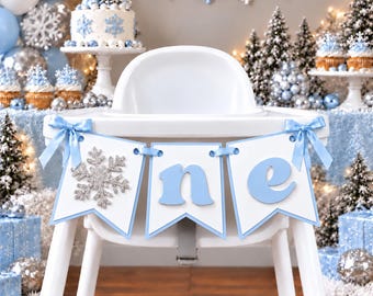 Peut inclure: Une chaise haute blanche décorée d'une bannière avec un flocon de neige à paillettes argentées et les lettres bleu clair O, N et E. La bannière est fixée avec des rubans de satin bleu clair de chaque côté pour un décor hivernal.