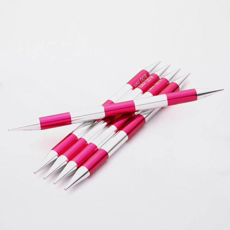 May include: Set of six pink and silver knitting needles, each needle is 800 mm long. The needles are arranged in a stack with the tips pointing in different directions.