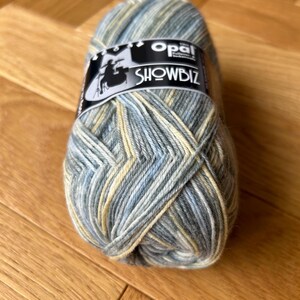 May include: A ball of Opal Showbiz yarn in a blue, green, and yellow colourway. The yarn is a blend of wool and nylon.