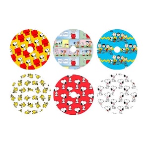 May include: Six round vinyl stickers featuring different Peanuts characters and designs. The stickers feature Snoopy, Woodstock, Charlie Brown, Lucy, and Linus. The stickers are in a variety of colours, including red, yellow, blue, and white.