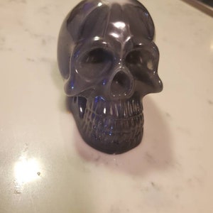 May include: A black and silver skull figurine with a glossy finish. The skull has a detailed face with a prominent nose and teeth.