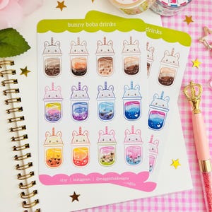 May include: A sheet of 18 stickers featuring cute bunny-themed boba drinks. The stickers are arranged in three rows of six. Each sticker features a different color and flavor of boba drink. The stickers are printed on white paper with a green border. The text "bunny boba drinks" is printed at the top of the sheet. The text "etsy | instagram | @maggiefuldesigns" is printed at the bottom of the sheet.