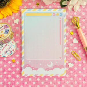 May include: A pastel-colored notepad with a grid pattern, designed with a dreamy aesthetic. The notepad features a cloud and star motif at the bottom, with a window-like frame. Decorative washi tape, a pen, and paperclips are also visible.