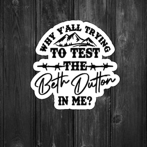 May include: A black and white sticker with the text "Why y'all trying to test the Beth Dutton in me?" and a cartoon pig wearing a sunflower. The sticker is on a dark wood grain background.