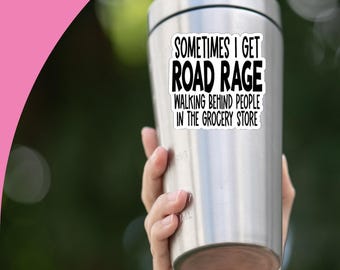 May include: A stainless steel tumbler with a black lid, held by a hand. The tumbler has a sticker that reads "SOMETIMES I GET ROAD RAGE WALKING BEHIND PEOPLE IN THE GROCERY STORE". A cartoon pig with a sunflower is in the upper left.