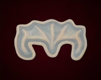 May include: A white ceramic mold shaped like a bat with a textured surface. The mold is designed for making cookies or other baked goods.