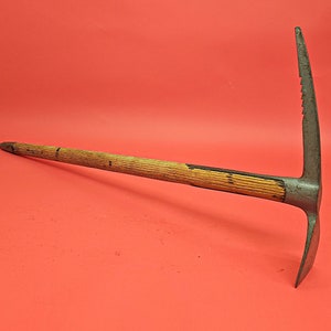 Op de afbeelding: Een vintage ijsbijl met een houten steel en een metalen kop. De kop heeft een gekartelde rand en een puntige punt.