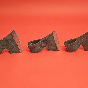 May include: Three small, hand-forged axes with wooden handles. The axes are made of metal and have a dark brown finish. The axes are arranged in a row on a red background.