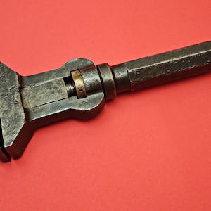 Könnte beinhalten: Ein vintage verstellbarer Schraubenschlüssel mit schwarzer Metalloberfläche und einer Messing-Einstellschraube. Der Schraubenschlüssel hat einen langen Griff und einen festen Backen.