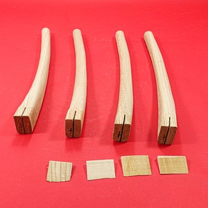 May include: Four wooden chair legs with a curved shape and a notch at the bottom. Four small wooden pieces are also shown.