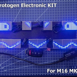 Peut inclure: Un kit électronique MK5 Protogen pour base M16 MK5 comprenant plusieurs panneaux d'affichage à matrice LED bleue reliés par des câbles plats, une petite télécommande noire avec quatre boutons A, B, C, D et un module de contrôle noir.