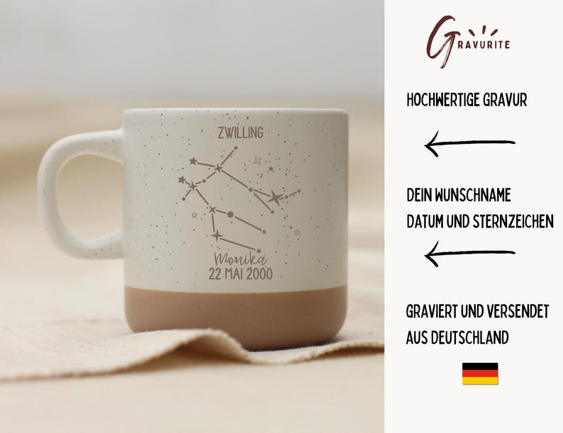 May include: A speckled ceramic mug with a white handle and a tan base. The mug features an engraved Gemini constellation design, the name "Monika", and the date "22 MAI 2000".