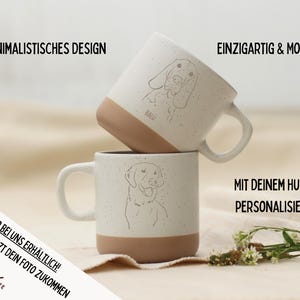 May include: Two white ceramic mugs with a speckled finish and tan bottoms. Each mug features a line drawing of a dog's face. The text on the mugs says "Minimalist Design", "Unique & Modern", and "Personalized with your dog".